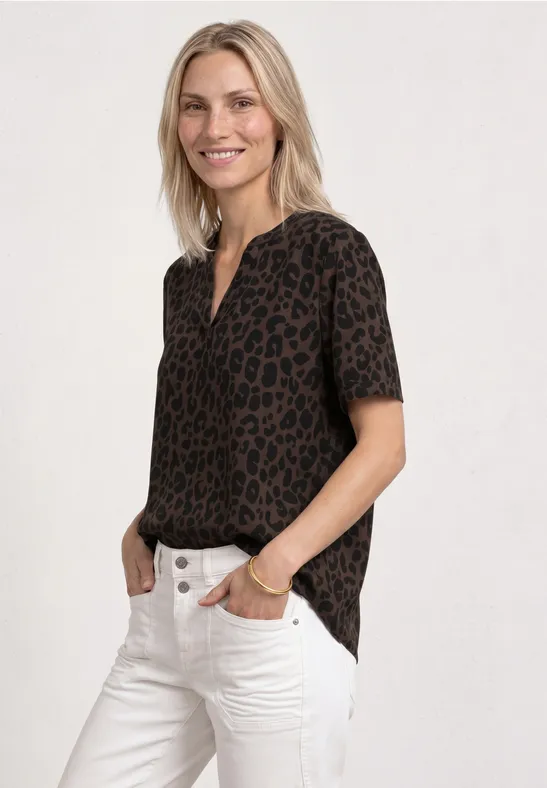 Vrouw met kort mouw luipaardprint blouse en witte jeans, handen in de zakken.