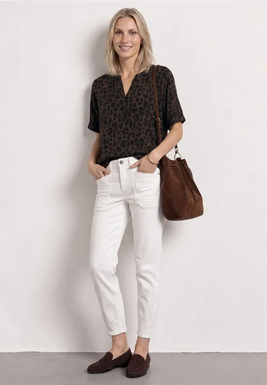 Vrouw draagt gemêleerd shirt, witte slim-fit broek, bruine mules en bijpassende schoudertas tegen witte achtergrond.