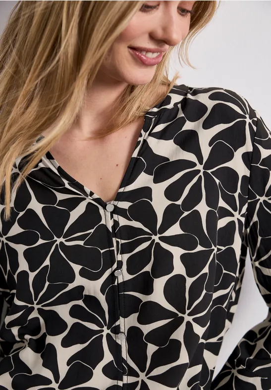 Dame trägt weiße Bluse mit schwarzem, großflächigem Blumenmuster und V-Ausschnitt.