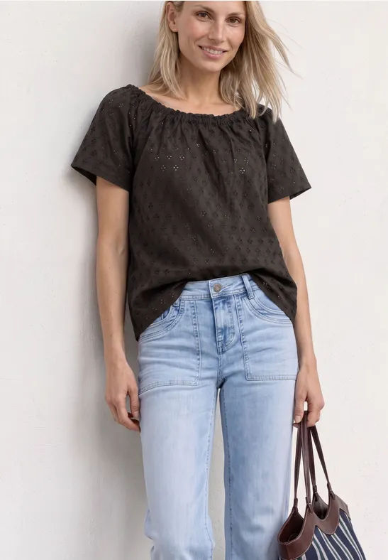 Vrouw met zwarte blouse, lichtblauwe jeans en bruine tas voor een witte achtergrond.