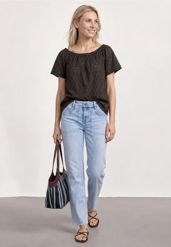 Vrouw in zwart t-shirt, lichtblauwe jeans, sandalen en een gestreepte tas.
