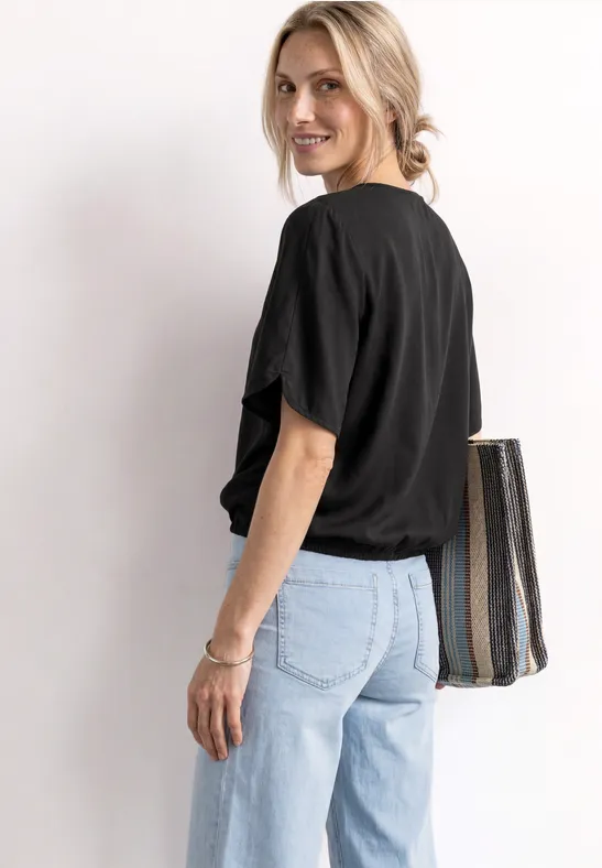 Person in schwarzem T-Shirt und hellblauen Jeans, trägt eine gestreifte Tasche über der Schulter.