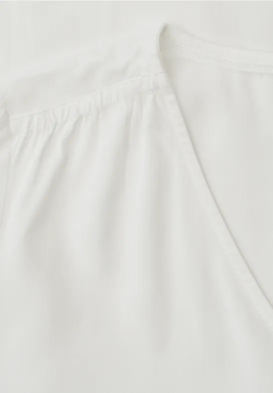 Weiße Bluse mit V-Ausschnitt und leichten Falten am Schulterbereich.