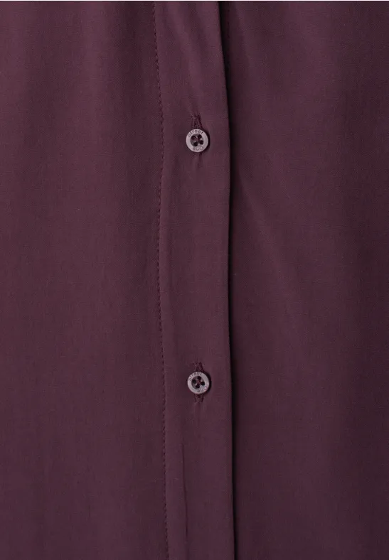 Close-up van een bordeauxrode blouse met knoopsluiting en twee knopen
