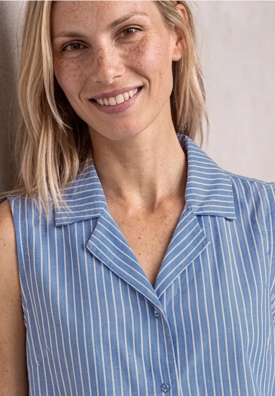 Glimlachende vrouw met sproeten en licht haar in een mouwloze, blauw-wit gestreepte blouse.