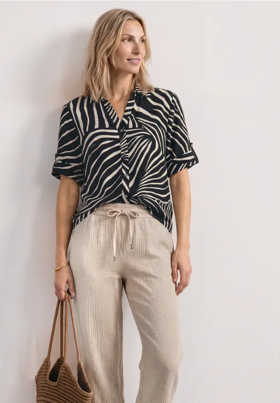 Vrouw met zwart-wit gestreepte top, beige linnen broek en bruine tas.