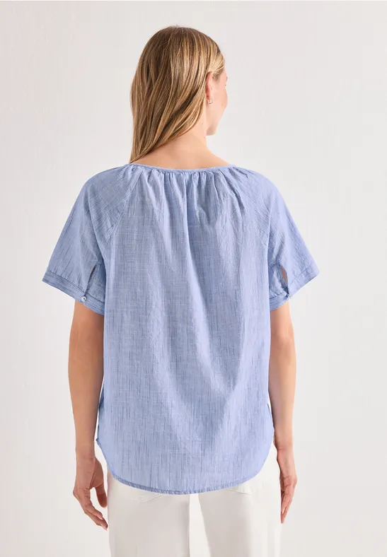 Vrouw van achteren gezien in een lichtblauw T-shirt met korte mouwen en fijne strepen.
