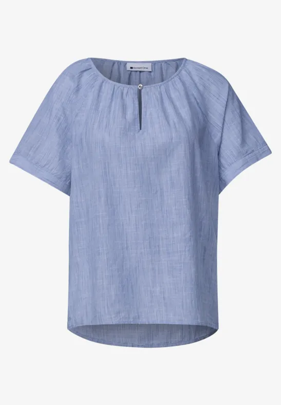 Lichtblauwe, losse blouse met korte mouwen, ronde hals met splitje en subtiele geweven structuur.