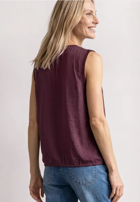 Eine Frau von hinten in ärmellosem bordeauxfarbenem Top und Jeans.