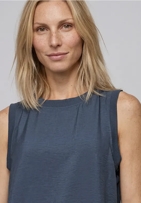 Blondynka w ciemnym, bezrękawnikowym topie na jasnym tle.