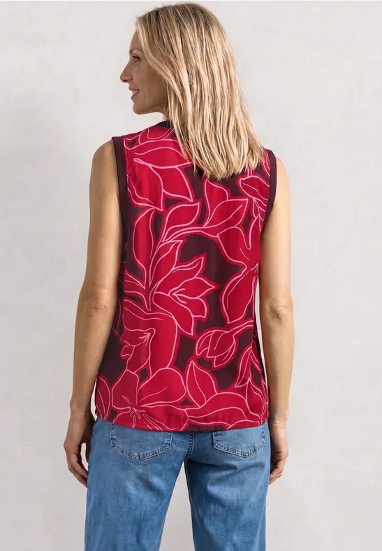 Vrouw van achteren in rode mouwloze top met bloemenprint en blauwe spijkerbroek.