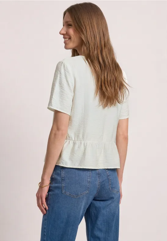 Frau von hinten in weißem Kurzarmshirt mit Rüschenbund und blauen Jeans.