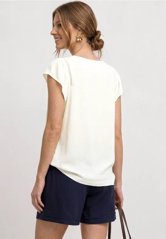 Eine Frau von hinten trägt weißes Shirt, blaue Shorts und hält eine Handtasche.