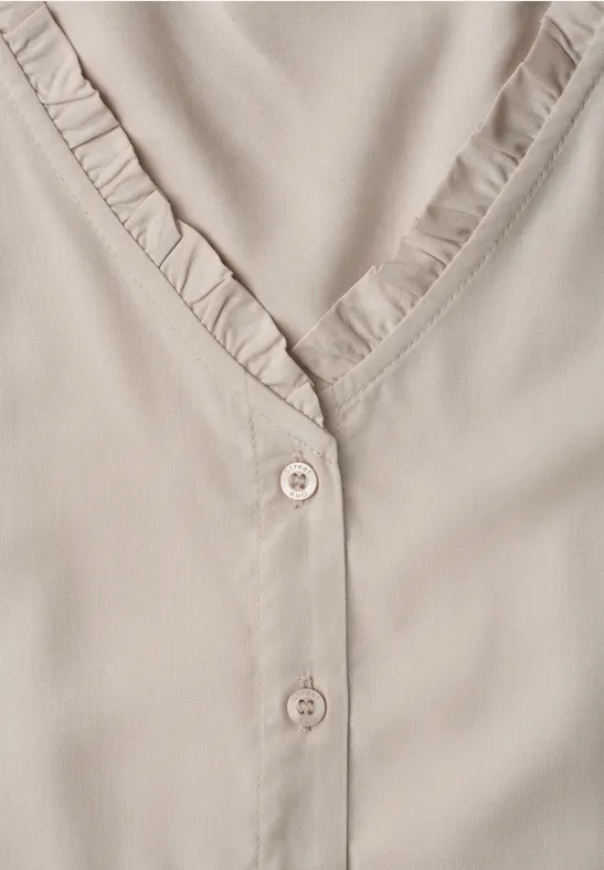 Beige blouse met V-hals, ruches langs de kraag en twee subtiele knoopjes.