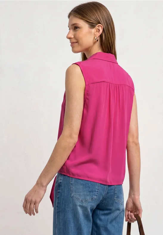 Frau von hinten in pinker ärmelloser Bluse und blauen Jeans, in der Hand eine kleine Clutch.