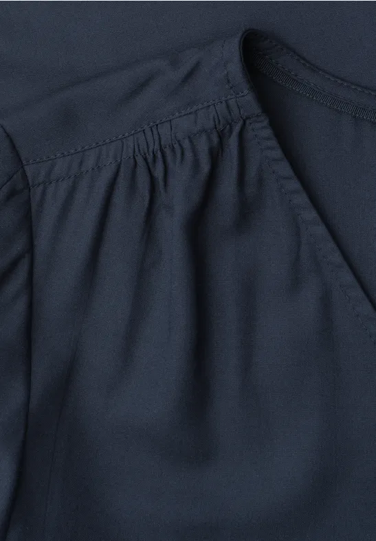 Donkerblauw kledingstuk met zakopening en fijne plooien.