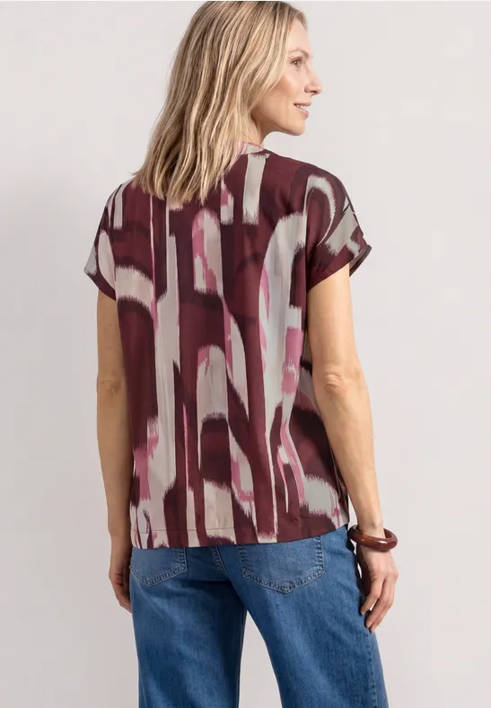 Een vrouw van achteren in een rood-wit patroonshirt met korte mouwen en een blauwe spijkerbroek.