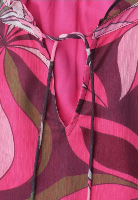 Close-up van een roze-bordeaux top met golvend retroprint en strikje bij de hals.