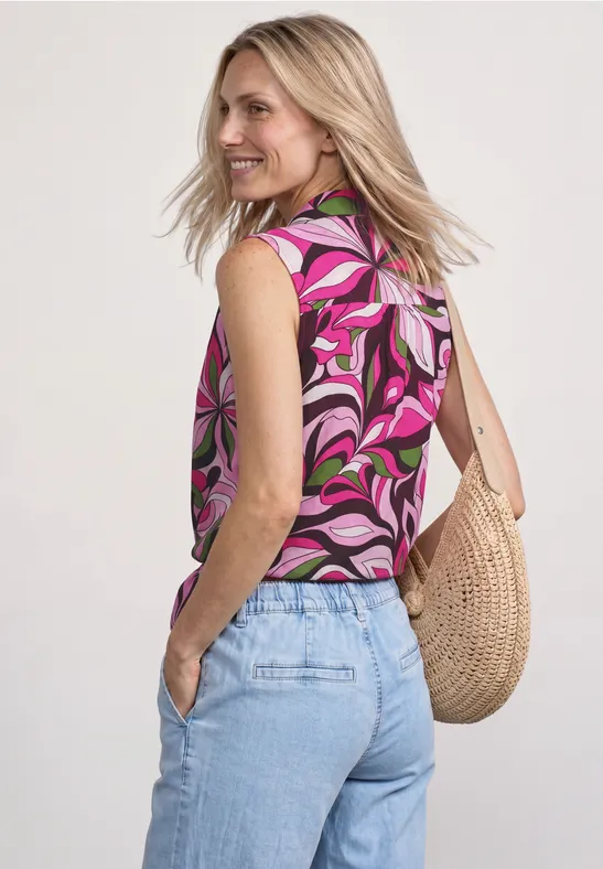 Frau von hinten mit pinkem, gemustertem Top, hellblauen Jeans und einer Strohtasche.
