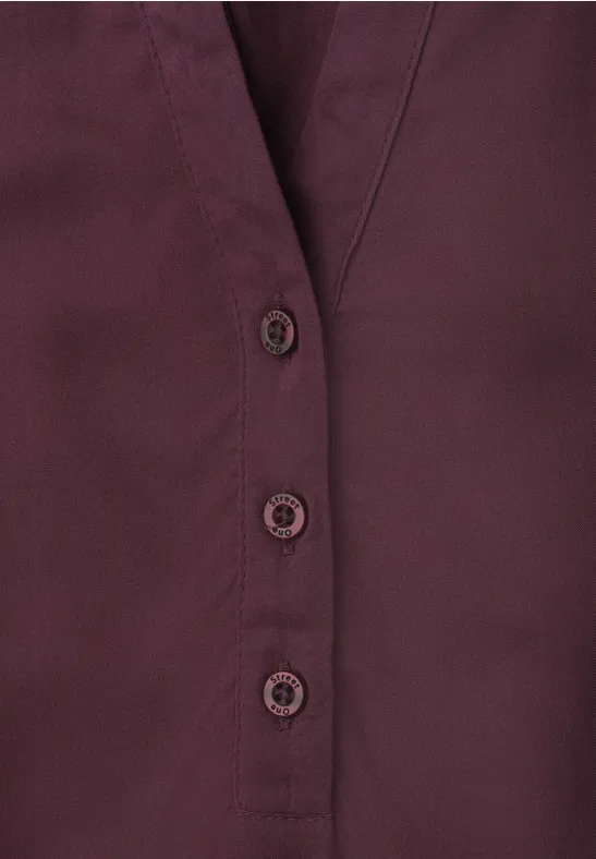 Donkerrode blouse met V-hals en drie zichtbare knopen.