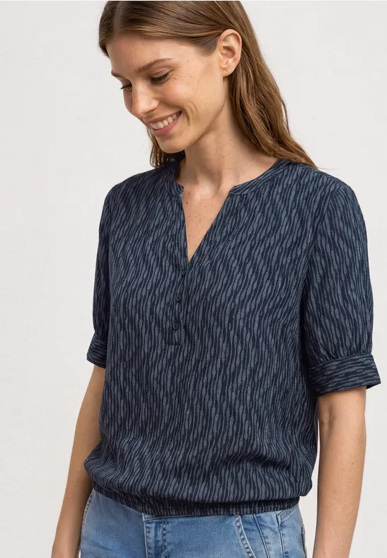 Een vrouw draagt een donkerblauwe blouse met subtiel patroon en driekwart mouwen.
