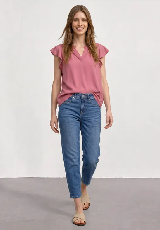 Jeune femme en jean et top rose, souriante en studio.