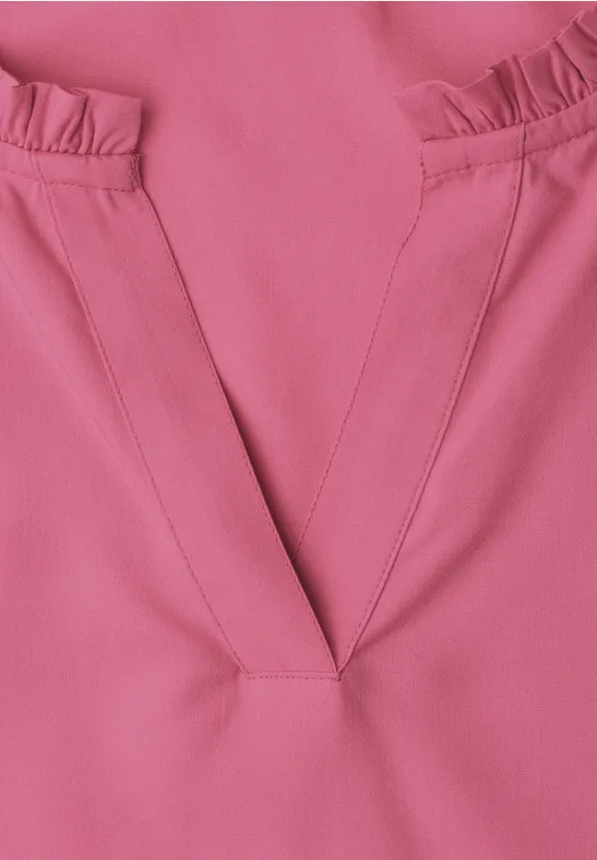 Gros plan d’un haut rose avec un col en V et des volants sur les épaules.