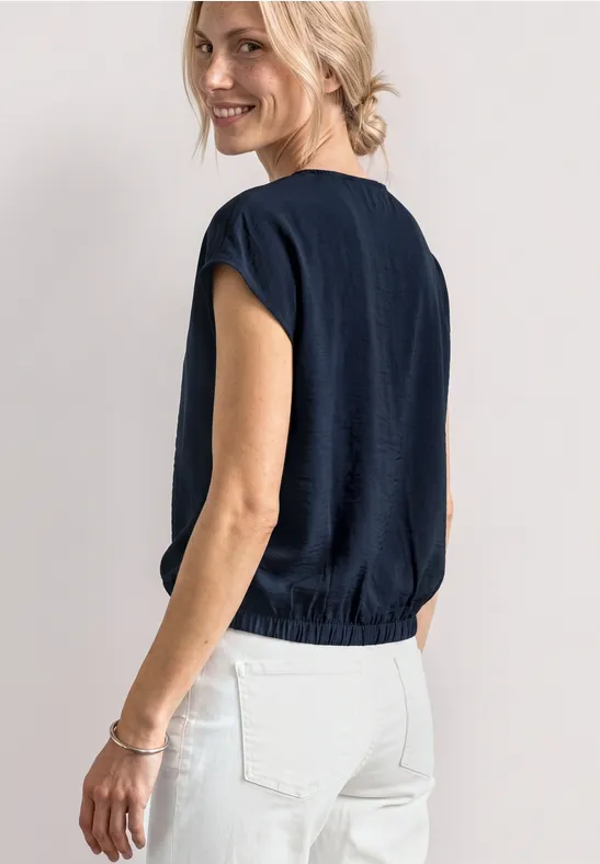 Achteraanzicht van vrouw in donkerblauw kort T-shirt en witte broek, haar in een knot.