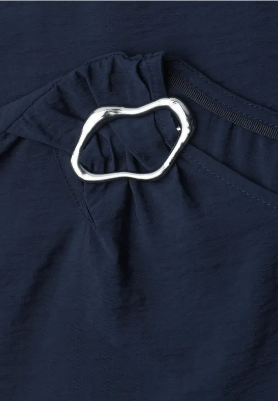 Donkerblauw textiel met een zilverkleurige, organisch gevormde ring als sierdetail bij een plooi.