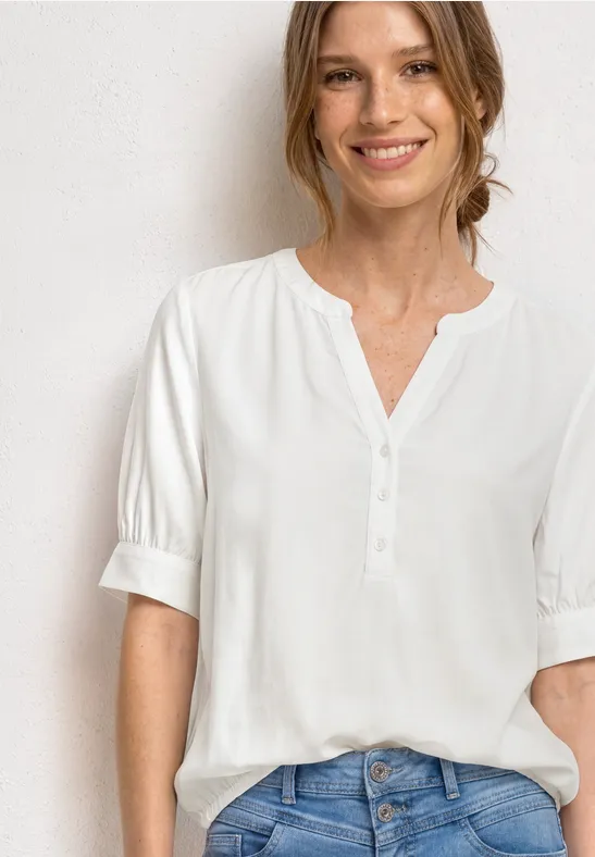 Femme en chemisier blanc à manches mi-longues avec patte de boutonnage, porté sur jean.