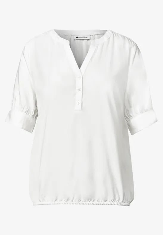 Blouse blanche col en V avec patte de boutonnage courte et ourlet élastiqué.