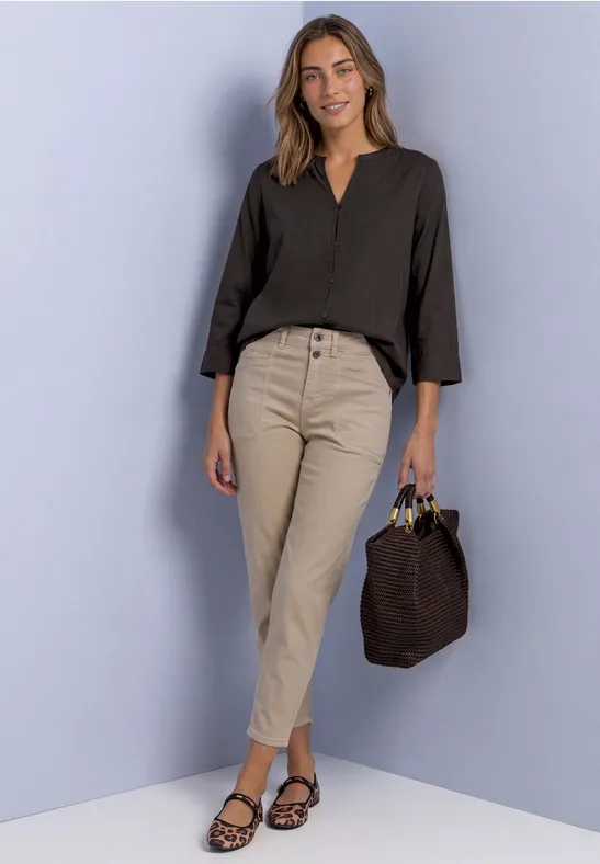 Une femme souriante porte un chemisier noir, un pantalon beige, des sandales et un sac brun.