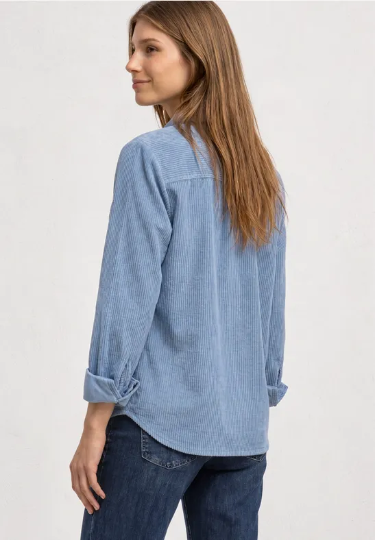 Eine Frau mit langem Haar in blauer Jeansbluse und Jeans, von hinten, schaut seitlich.
