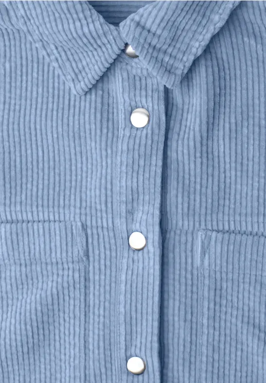Nahaufnahme eines hellblauen Cord-Hemds mit silbernen Druckknöpfen.