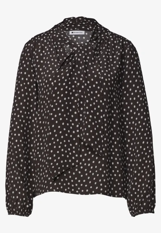 Blouse noire à manches longues à pois blancs avec nœud cravate au col.
