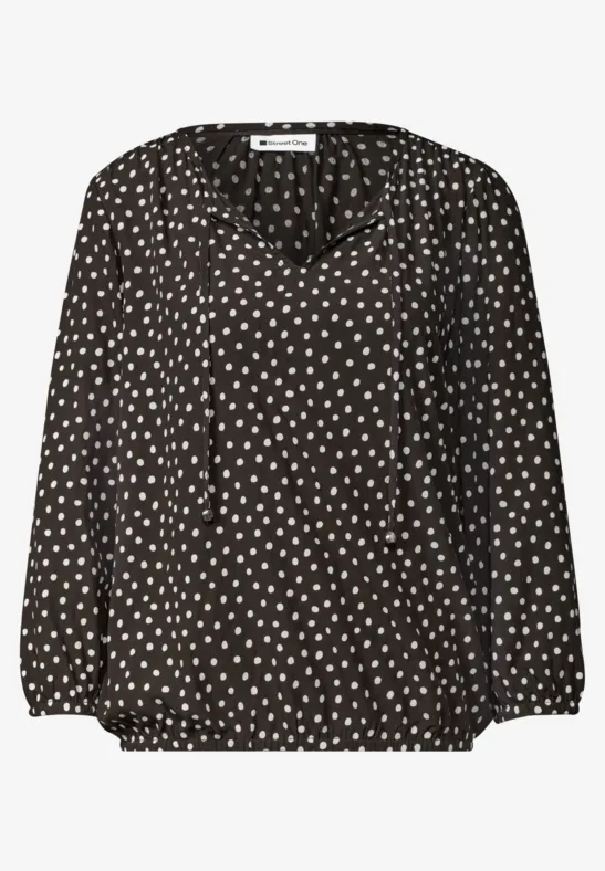 Schwarze Bluse mit weißem Herzpunkte-Muster, V-Ausschnitt und langen Ärmeln.