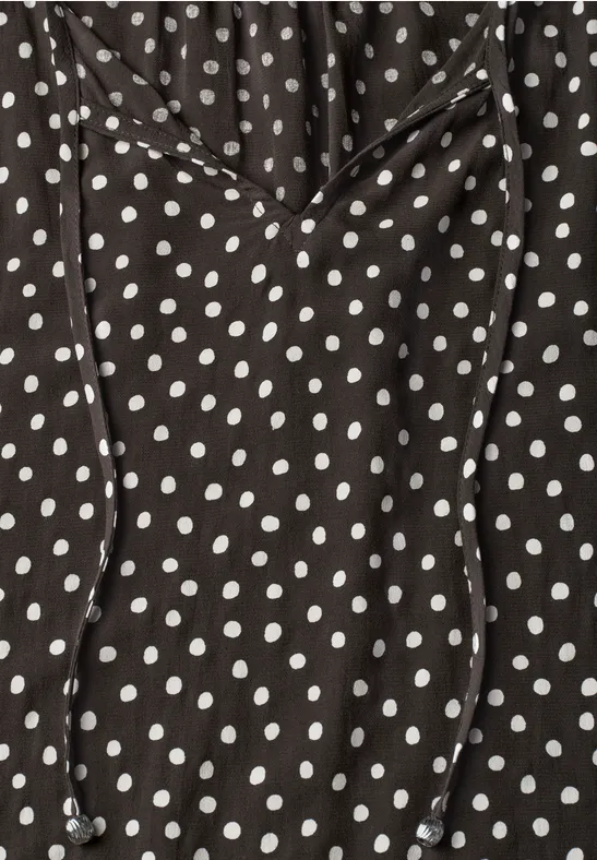 Schwarzes Kleidungsstück mit weißen Polka Dots und Kordelzug am Ausschnitt.