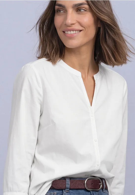 Femme en chemise blanche à manches retroussées et ceinture, visage souriant.