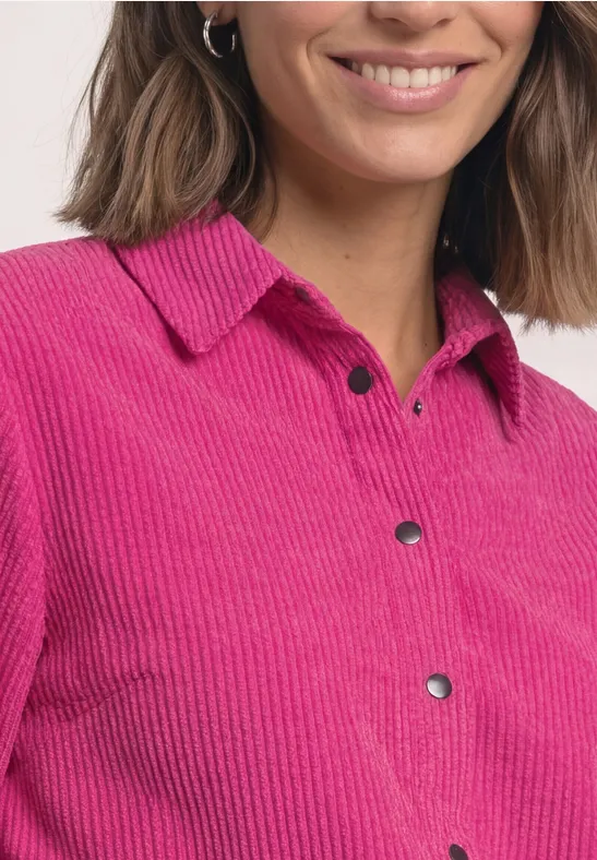 Une femme porte une chemise en velours côtelé rose à col et boutons-pression noirs.