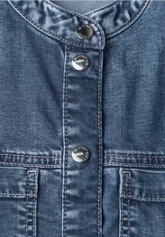 Naheansicht einer blauen Jeansjacke mit silbernen Druckknöpfen und zwei aufgesetzten Taschen.