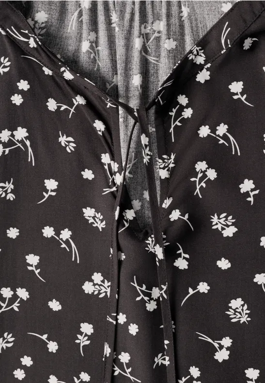Schwarze Bluse mit weißem Blumenmuster und Bindeband am Ausschnitt.