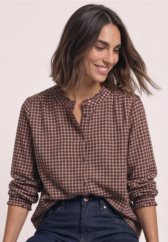 Femme portant une chemise marron à carreaux, souriante face à l'objectif.