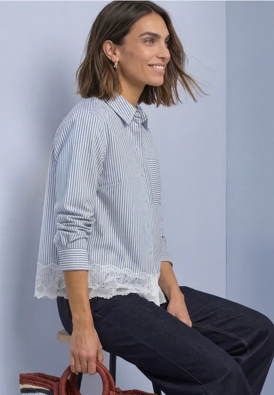 Femme aux cheveux mi-longs en chemise rayée bleu-blanc à dentelle, assise de profil sur un tabouret.