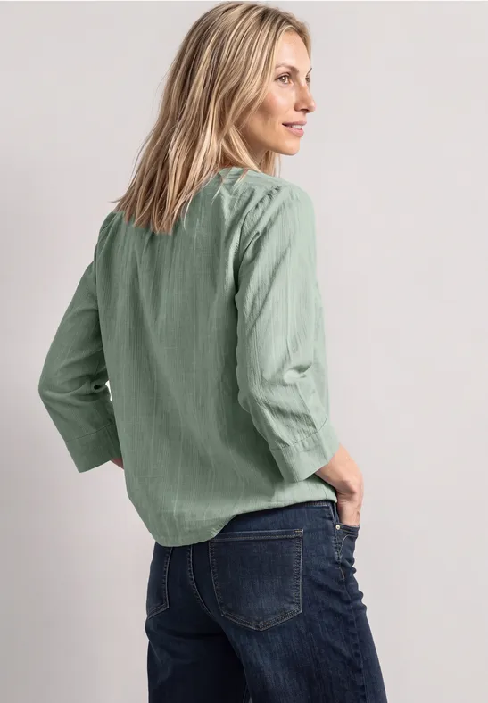 Vrouw in profiel met groene blouse en blauwe spijkerbroek