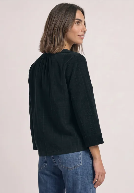 Vrouw schuin van achter, draagt een zwart gestructureerd shirt en een blauwe spijkerbroek, kijkt over haar schouder.