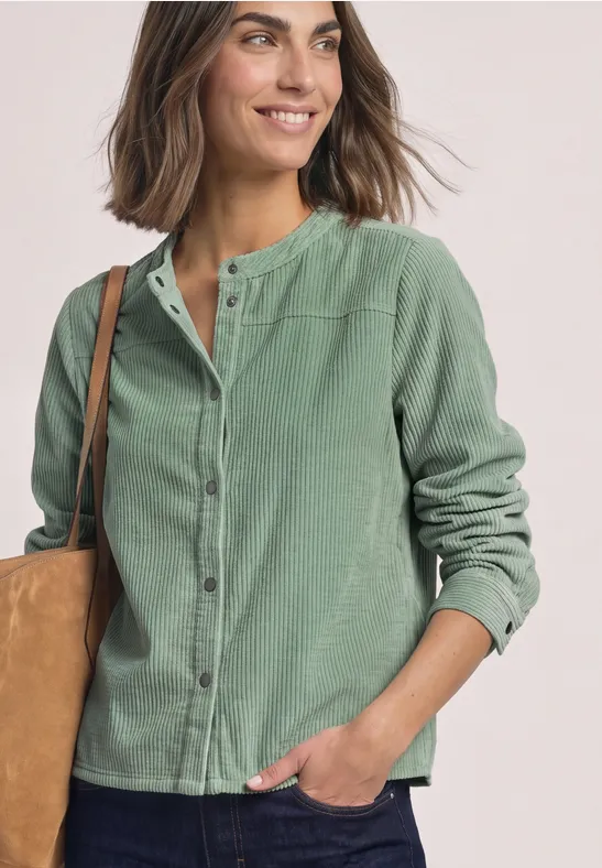 Femme souriante en chemise-veston verte avec sac sur l’épaule.