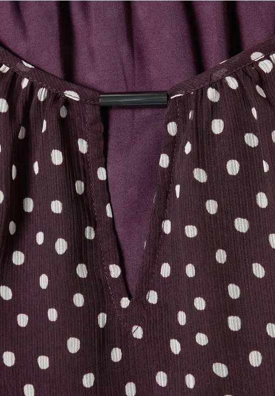 Haut violet à pois blancs et encolure en V.