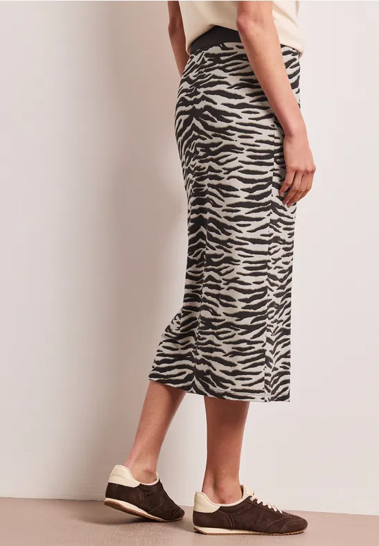 Une femme porte une jupe midi à imprimé zèbre noir et blanc, associée à des baskets marron.