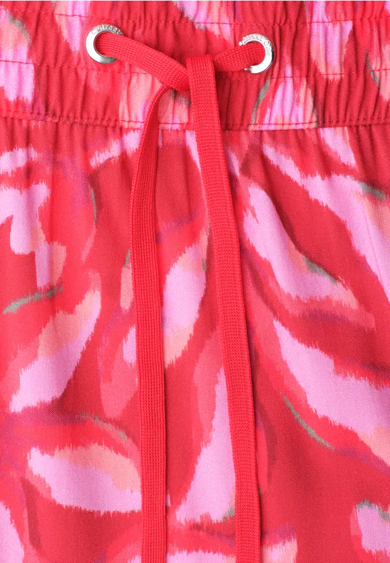 Roter Stoff mit rosa-weißen abstrakten Mustern, elastischer Bund mit roter Kordel und Ösen.