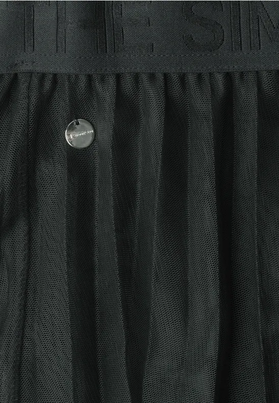 Schwarzer Tüllrock mit transparenten Falten, elastischem Bund und rundem Metall-Emblem.